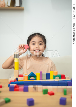 Cheerful Young Girl Engaging in Creative Play with Colorful Wooden Building Blocks on a Table at Home, Focused on Imagination and Learning Cheerful Young Girl Engaging in Creative Play with Colorful Wooden Building Blocks on a Table at Home, Focused on Imagination and Learning 132935811