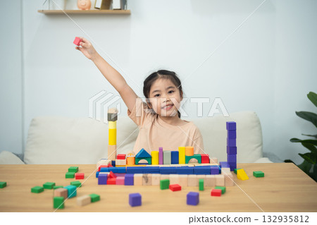Happy child playing with colorful building blocks at home, creating structures and learning through play in a bright and inviting environment Happy child playing with colorful building blocks at home, creating structures and learning through play in a bright and inviting environment 132935812