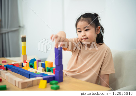 Young Girl Stacking Colorful Building Blocks in Bright Room, Engaged in Educational Playtime Activity, Developing Creativity and Motor Skills Young Girl Stacking Colorful Building Blocks in Bright Room, Engaged in Educational Playtime Activity, Developing Creativity and Motor Skills 132935813
