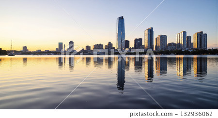Cityscape Reflection Water Dawn Panoramic view of a modern city skyline silhouetted against a soft dawn sky, perfectly reflected 132936062