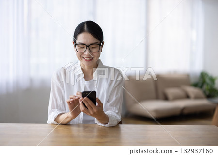 一位戴著眼鏡的中年婦女微笑著操作智慧型手機。 132937160