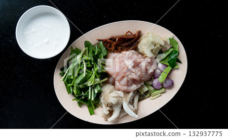 Top view of material for made Tom Kha Kai cut into pieces. With Raw chicken, galangal, lemongrass, kaffir lime leaves and mushroom, Tamarind paste. And With coconut milk in a cup. Arranged on a plate. Top view of material for made Tom Kha Kai cut into pieces. With Raw chicken, galangal, lemongrass, kaffir lime leaves and mushroom, Tamarind paste. And With coconut milk in a cup. Arranged on a plate. 132937775