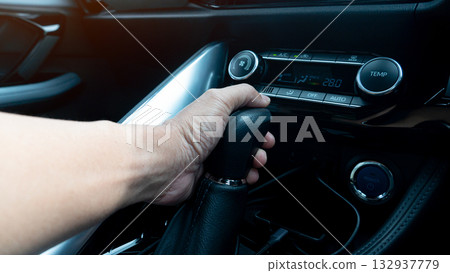Close up of hand that controls the automatic gear lever. Grip to control the car to move forward for electric gear. Interiro of car with dark tone. Close up of hand that controls the automatic gear lever. Grip to control the car to move forward for electric gear. Interiro of car with dark tone. 132937779
