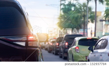 Rear side of car with turn on brake light. Cars parked in long lines in the city. Green ornamental trees. With light shining from the front. 132937784