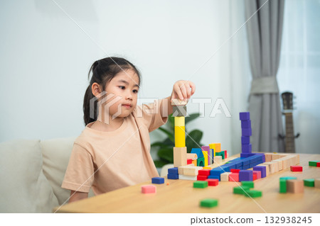 Young girl engaging in creative play with colorful building blocks, developing fine motor skills, and enhancing cognitive abilities in a bright room 132938245