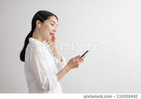Profile of a smiling middle-aged woman wearing wireless earphones and operating a smartphone Profile of a smiling middle-aged woman wearing wireless earphones and operating a smartphone 132938492