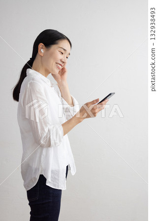 Profile of a smiling middle-aged woman wearing wireless earphones and operating a smartphone 132938493