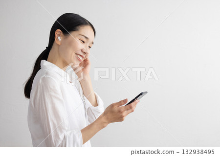 一位微笑的中年女性戴著無線耳機，正在操作智慧型手機。 132938495