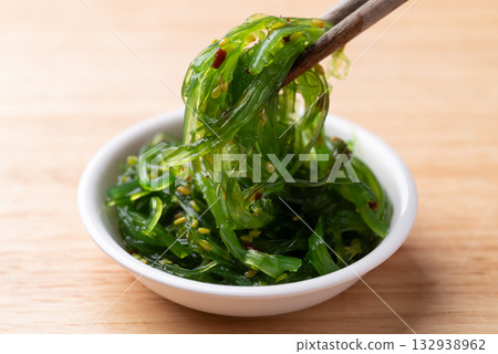Wakame seaweed salad with sesame seed in a bowl with chopsticks on wooden background 132938962