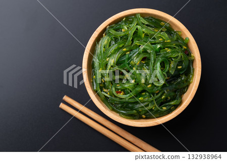 Wakame seaweed salad with sesame seed in a wooden bowl with chopsticks on black background, Top view 132938964