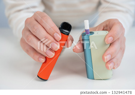 Woman holding electronic cigarette and disposable vape on white background. Tobacco heating systems and vaporizer.  132941478