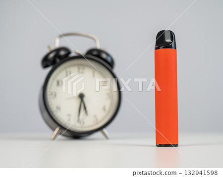 Disposable vape and alarm clock on white background.  132941598