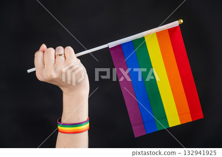 Woman with wedding ring holding rainbow flag on black background. Woman with wedding ring holding rainbow flag on black background. 132941925