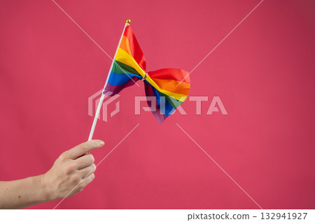 Woman holding rainbow flag fastened with wedding ring on pink background. Woman holding rainbow flag fastened with wedding ring on pink background. 132941927