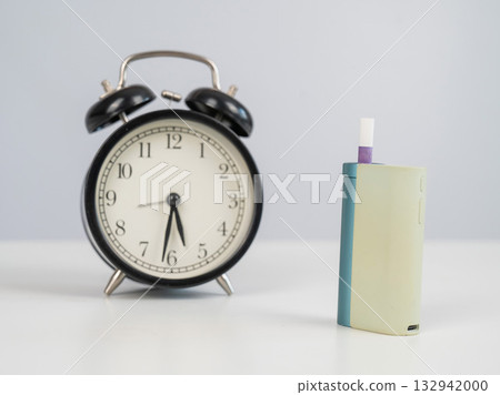 Electronic cigarette and alarm clock on white background. Tobacco heating systems. Electronic cigarette and alarm clock on white background. Tobacco heating systems. 132942000