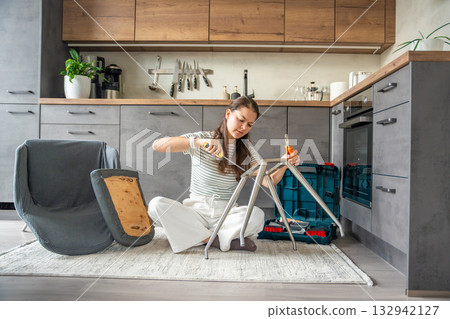 Young woman sitting on the floor assembling a chair with tools. Concept of female independence and do it yourself lifestyle. 132942127