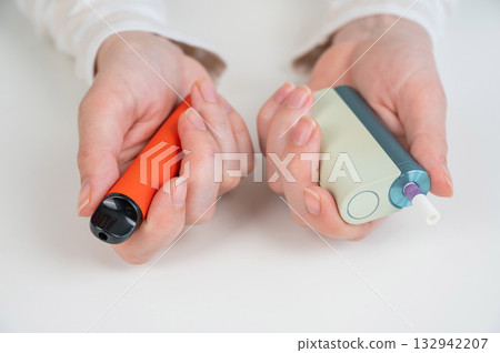 Woman holding electronic cigarette and disposable vape on white background. Tobacco heating systems and vaporizer. Woman holding electronic cigarette and disposable vape on white background. Tobacco heating systems and vaporizer. 132942207