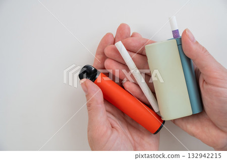 Woman holding regular, electronic cigarette and disposable vape on white background. Tobacco heating systems. Woman holding regular, electronic cigarette and disposable vape on white background. Tobacco heating systems. 132942215