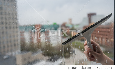 A woman washes a window with a special scraper.  132942284