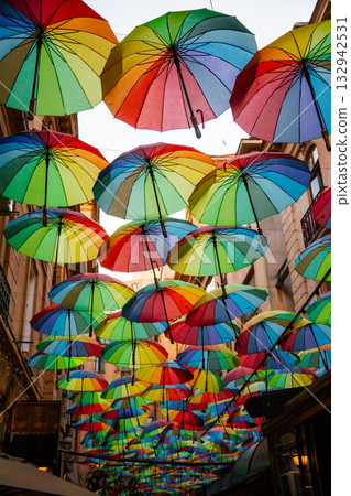 Colorful umbrellas create a vibrant atmosphere in a narrow street in an urban area during dusk Colorful umbrellas create a vibrant atmosphere in a narrow street in an urban area during dusk 132942531