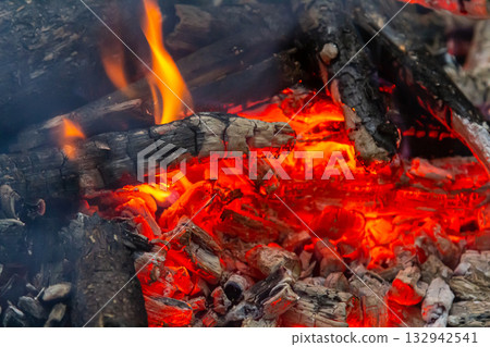 Glowing embers and flickering flames create a warm atmosphere in a campfire setting during a cool evening gathering Glowing embers and flickering flames create a warm atmosphere in a campfire setting during a cool evening gathering 132942541