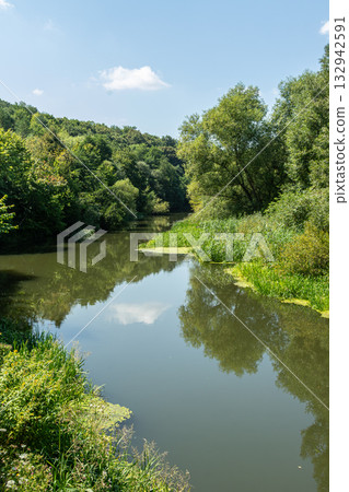 Serene river surrounded by lush greenery in a tranquil natural setting during a sunny day 132942591