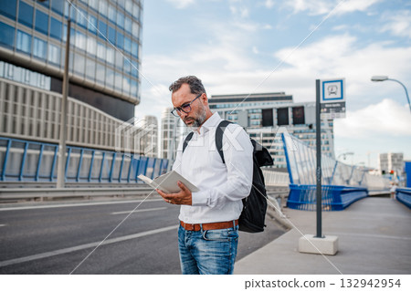 Mature man reading while waiting for bus. 132942954