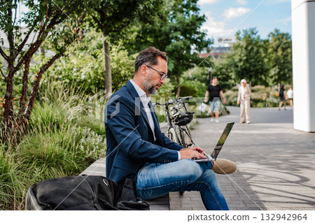 Manager working in urban park, making phone call and typing on laptop. Manager working in urban park, making phone call and typing on laptop. 132942964