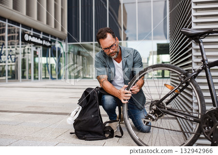 Man fixing bicycle wheel outdoors. 132942966
