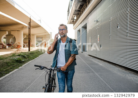 Male cyclist making phone call, standing by his bike. Male cyclist making phone call, standing by his bike. 132942979