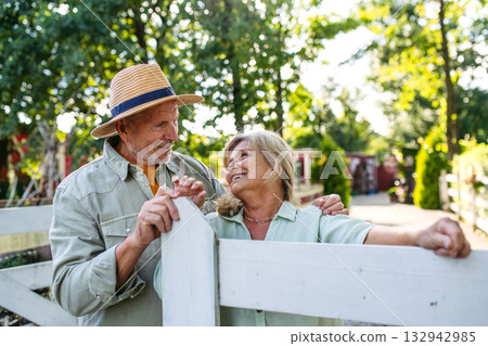 Happy elderly couple standing by white fence. 132942985