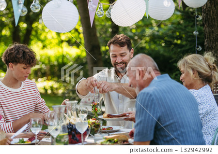 Family sharing food during garden grill party. 132942992