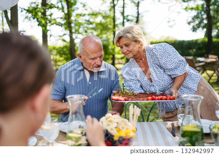 Senior woman serving grilled food during family grill party. Senior woman serving grilled food during family grill party. 132942997