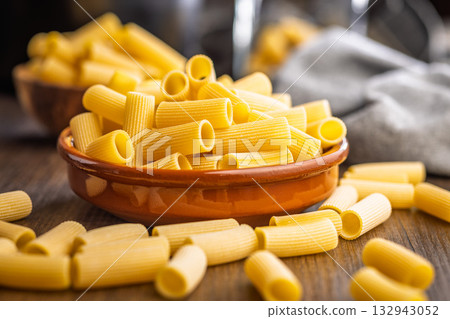 Uncooked rigatoni pasta in bowl on wooden table. Uncooked rigatoni pasta in bowl on wooden table. 132943052