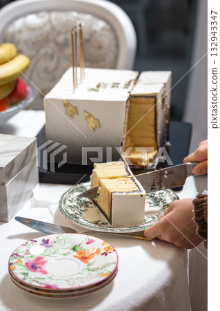 Hands slicing elegant white cake with gold rocket topper at celebratory event 132943347