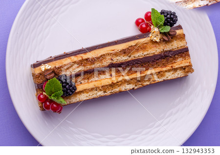 Layered chocolate and caramel cake slice with berries and gold leaf on white plate Layered chocolate and caramel cake slice with berries and gold leaf on white plate 132943353
