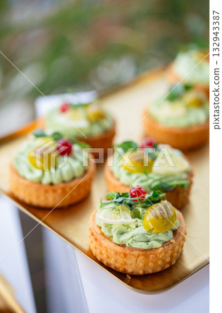 Elegant tartlets with creamy herb filling and pickle garnish on golden tray at outdoor event 132943387