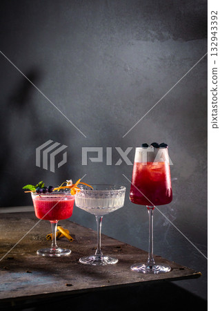 Three artisanal cocktails with berry and citrus garnish on moody metal surface Three artisanal cocktails with berry and citrus garnish on moody metal surface 132943392