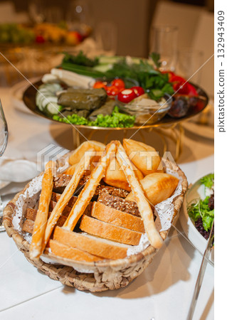 Rustic bread basket with assorted loaves and baguettes beside vegetable platter 132943409