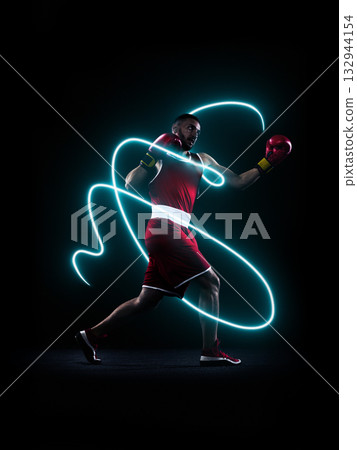 Professional boxer in red gloves throwing punch with bright neon energy trail in dark studio Professional boxer in red gloves throwing punch with bright neon energy trail in dark studio 132944154