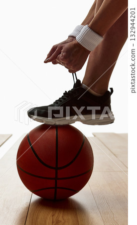 Athlete tying shoelace with foot resting on basketball for balance 132944201