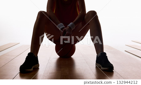 Female basketball player sitting with ball between knees in focus moment 132944212