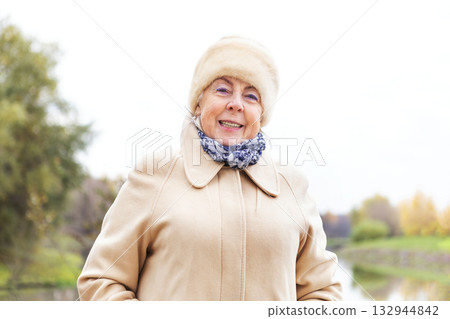 Happy senior woman in warm coat and fur hat on an autumn day. Smiling caucasian businesswoman. Retired female portrait for advertising. 132944842