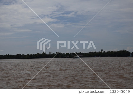 A view of the Mekong River from a boat, showing the river surface, boats, green forests, land and sky 132945049