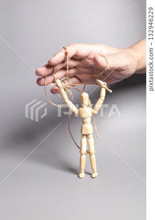 Man's hand pulling strings of wooden puppet on gray background. Concept of emotional manipulation,dictatorship and control Man's hand pulling strings of wooden puppet on gray background. Concept of emotional manipulation,dictatorship and control 132946229