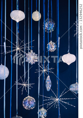 Hanging crystal and glass Christmas ornaments with starburst lights on a dark blue backdrop. Iridescent ornaments, celestial holiday trend, crystal starburst lights, cosmic Christmas 132946252