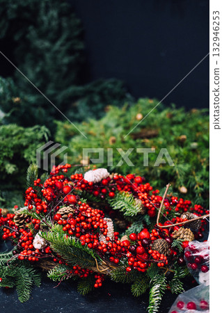 A festive wreath made of red berries, pinecones, and evergreen branches resting on a bed of greenery. Organic Christmas decor, wild winter wreaths, natural materials, rustic elegance 132946253