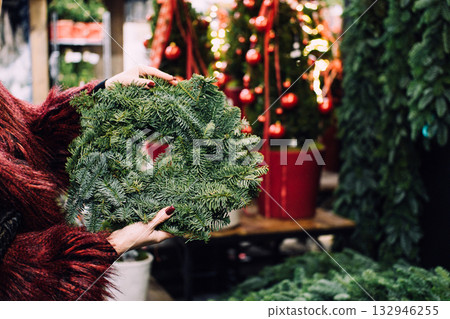 A female hand holds a natural pine wreath at a holiday market. Eco-friendly holidays, handmade traditions, Christmas preparation, sustainable design 132946255