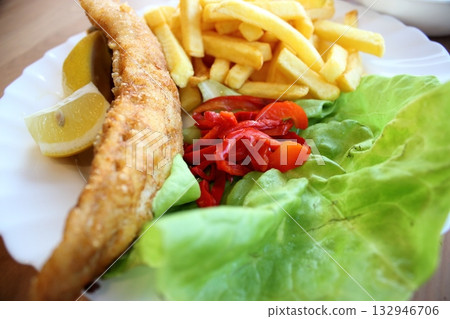 Fried fish fillet with fries, lettuce and red pepper 132946706