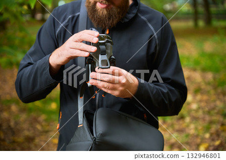 In a lush green park, a man adjusts his camera while standing among fallen leaves and vibrant trees. He focuses on capturing the beauty around him. In a lush green park, a man adjusts his camera while standing among fallen leaves and vibrant trees. He focuses on capturing the beauty around him. 132946801